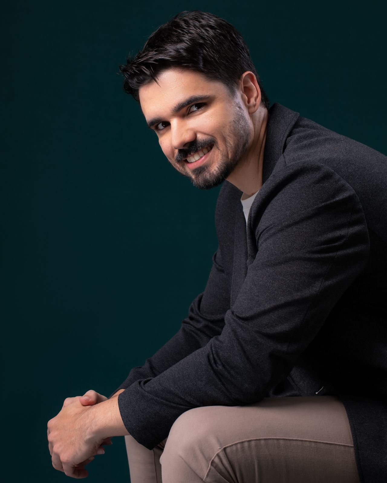Maycon Gabry sorrindo, sentado, em fundo verde escuro